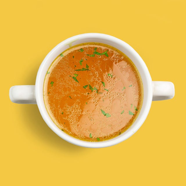 bowl of fresh chicken broth isolated on yellow background, top view