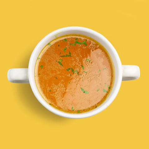 bowl of fresh chicken broth isolated on yellow background, top view