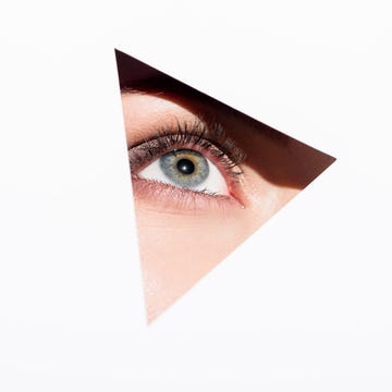 close up shot of woman looking out of hole with one eye isolated on white