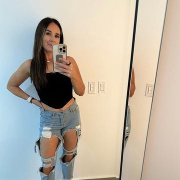 person posing in a mirror wearing a black top and ripped jeans