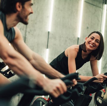 shot of two young people exercising on exercise bike at gym. young man and young woman riding cycling machines in the gym. athletic couple of cyclists train on static bicycle simulator.