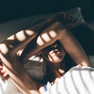 woman lying in bed with arms over her eyes