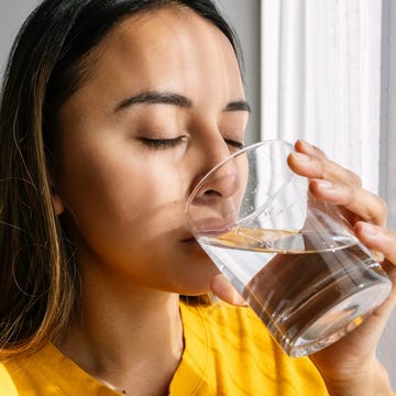 young latin american woman drinking a glass of fresh water standing close to the window in the morning. healthy lifestyle and people concept.