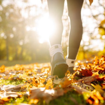 close up of female legs in hiking boots walks on ground with yellow orange dry fall leaves during autumn season in park or forest. feet walking in outdoor nature. healthy lifestyle on leisure activity
