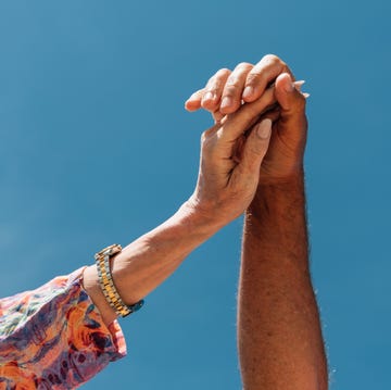 a heartfelt close up of two mature hands reaching up and interlocking against a vivid blue sky. the image captures the essence of connection, love, and trust between an older couple.
