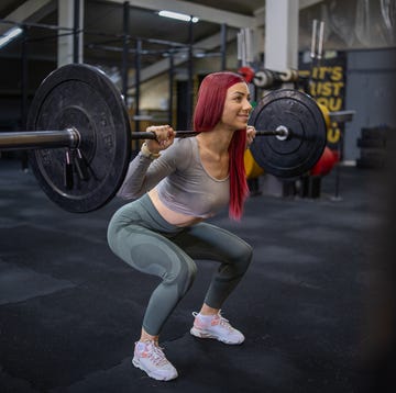 athlete girl with red hair doing squats with a barbell in the gym. she development of leg muscles and strengthening of the spine.