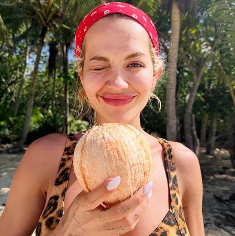 person holding a coconut on a beach with palm trees in the background