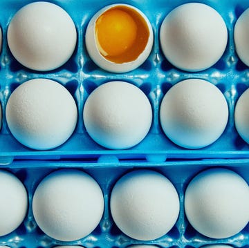 carton containing eggs with one cracked open revealing the yolk