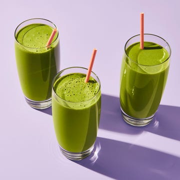 three glasses of green smoothie with pink straws on a purple surface