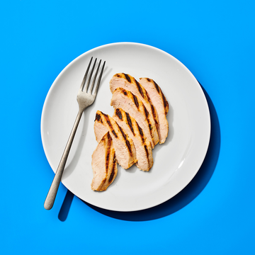 slices of chicken breast on a white plate with a silver fork, on a blue background
