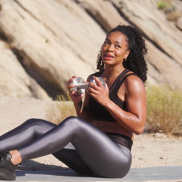 a person performing a workout outdoors sitting on a mat while holding dumbbells
